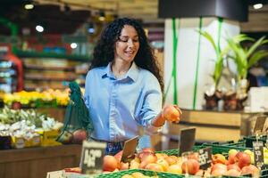 glimlachen Latijns Amerikaans bedrijf vrouw kiest en koopt vers appels, fruit in de supermarkt foto