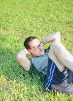 jong Mens met bril en groen t-shirt aan het doen sit ups en oefenen in park foto