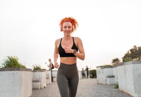 gelukkig jong roodharige sportvrouw jogging Aan voetpad foto