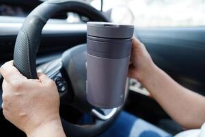 Aziatisch vrouw bestuurder houden ijs koffie kop en belegd broodje brood voor eten en drinken in auto, gevaarlijk en risico een ongeluk. foto