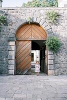 weinig meisje met een roze konijn komt uit van de gebogen houten deuren in de binnenplaats van een oude kasteel foto