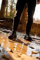 mannetje poten in zwart broek en sportschoenen tussen de plas en bevroren druppels in een overstroomd, vernietigd en verlaten huis. zonne- stralen. gevolgen van een natuurlijk ramp. foto