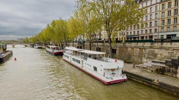 bewolkt dag over- de Seine rivier- in Parijs, met een afgemeerd rivierboot en vroeg voorjaar gebladerte voering de historisch steen kades, ideaal voor reizen en stedelijk thema's foto