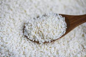 jasmijn witte rijst op houten lepel in de zak, oogst rijst en voedselkorrels kookconcept foto