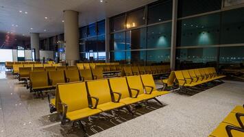 modern luchthaven vertrek lounge met leeg geel zitplaatsen en groot ramen Bij nacht, concept van reizen en vervoer foto