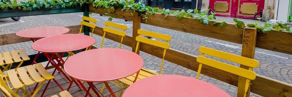 kleurrijk buitenshuis cafe instelling met rood tafels en geel stoelen Aan een geplaveide straat, ideaal voor concepten verwant naar zomer dining en Europese straat cafés foto