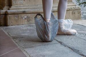 ballet artiest staand Aan haar tips terwijl vervelend plastic Tassen Aan haar schoenen. plastic Tassen zijn beschermen pointe schoenen Aan de straat. nieuw gebruik van plastic. voorbereidende werkzaamheden voor prestatie. achter de schermen. foto