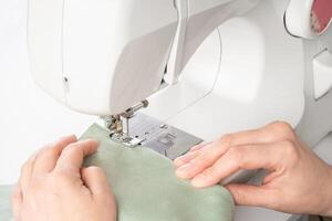 vrouw handen stiksels wit kleding stof Aan modern naaien machine Bij werkplaats in atelier foto
