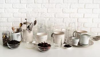 keramische en glazen kopjes en servies op tafel op witte bakstenen muur achtergrond foto