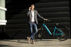 jonge zakenman die bij de ebike staat en mobiele telefoon gebruikt foto