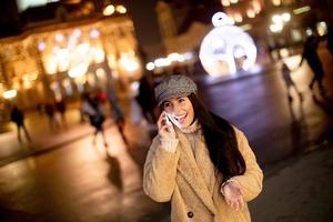 mooie jonge vrouw die haar mobiele telefoon op straat gebruikt in de kersttijd foto