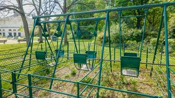 leeg groen metaal schommel rijden in een rustig park instelling, suggereren concepten van jeugd, nostalgie, en de buitenshuis Aan een helder zonnig dag foto