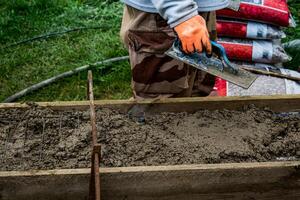 metselaar verspreiden beton met een troffel en niveau naar bouwen een muur Bij een bouw plaats foto