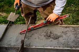 metselaar verspreiden beton met een troffel en niveau naar bouwen een muur Bij een bouw plaats foto