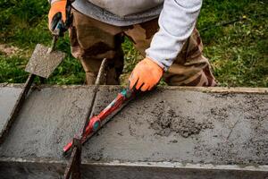 metselaar verspreiden beton met een troffel en niveau naar bouwen een muur Bij een bouw plaats foto