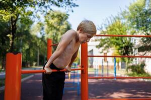 sportief jongen strekt zich uit omhoog en houdt Aan naar de bar met zijn handen. straat training Aan een horizontaal bar in de school- park. foto