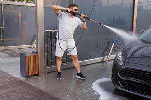 een Mens wast de voorkant van een auto met een water kanon. een auto Bij een zelf onderhoud auto wassen. foto