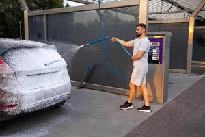 een Mens is van toepassing wasmiddel schuim naar de oppervlakte van een auto. een auto Bij een zelf onderhoud auto wassen. foto