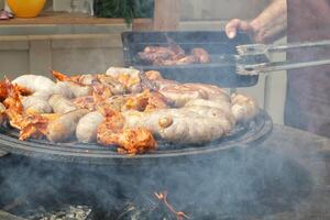 gebakken worstjes en kip Vleugels Aan barbecue rooster in de dorp. frituren vlees Aan Open brand. barbecue partij Aan achtertuin van land huis cabine. straat voedsel festival. huis Koken buitenshuis. picknick tijd foto