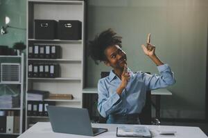 blij opgewonden succesvolle Aziatische zakenvrouw triomfeert met een laptopcomputer-smartphone op het kantoor op de werkplek foto