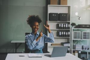 blij opgewonden succesvolle Aziatische zakenvrouw triomfeert met een laptopcomputer-smartphone op het kantoor op de werkplek foto