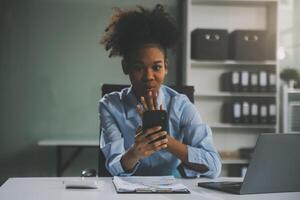 blij opgewonden succesvolle Aziatische zakenvrouw triomfeert met een laptopcomputer-smartphone op het kantoor op de werkplek foto