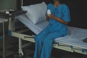jong vrouw zittend Aan de bed en op zoek buiten venster in ziekenhuis zich zorgen maken over haar ziekte. foto