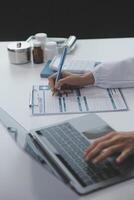 een professioneel en gefocust Aziatisch vrouw dokter in scrubs is werken en lezing medisch Onderzoek Aan haar laptop in haar kantoor Bij een ziekenhuis. foto