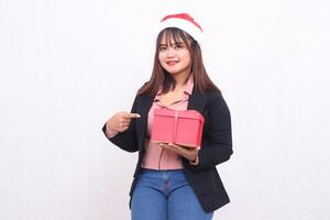 mooi Aziatisch meisje in vrolijk pak met de kerstman claus hoed poseren met Kerstmis geschenk doos en hand- tonen geschenk Aan wit achtergrond voor Promotie, reclame, banier, aanplakbord foto