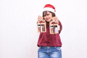 mooi jong zuidoosten Aziatisch vrouw glimlachen handen vooruit draag- 2 dozen van belemmeren cadeaus Bij Kerstmis vervelend de kerstman claus hoed modern rood overhemd kleding wit achtergrond voor Promotie en reclame foto