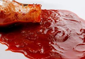 tomaat saus . een glas fles met ketchup en een plas van ketchup gemorst in de omgeving van het. foto