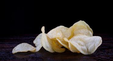 aardappel chips Aan een donker achtergrond. chips Aan een houten bord foto