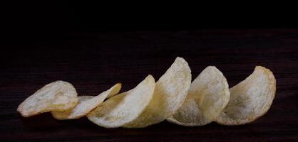 aardappel chips Aan een donker achtergrond. chips Aan een houten bord foto