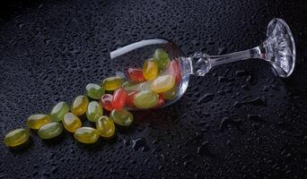 een veel van snoep wandelstokken zijn verspreide van een vernietigd glas beker. veelkleurig snoepjes in een glas Aan een zwart achtergrond. marmelade snoepjes. foto