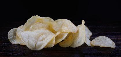 aardappel chips Aan een donker achtergrond. chips Aan een houten bord foto