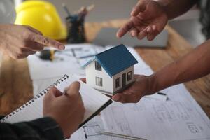 ingenieurs zijn overleg plegen de team naar ontwerp een bouwkundig structuur voor klanten met blauwdrukken en gebouw modellen naar werk Bij kantoor. foto