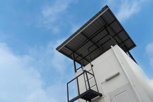 hoog gebouw met trap voor beklimming omhoog. de top is gedekt met een metaal kaas dak. voor opslaan water tanks en observatie locaties. onder blauw lucht en wit wolken. foto