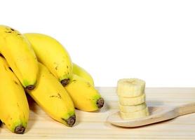 tros bananen op houten tafel naast lepel met gesneden fruit, witte achtergrond foto
