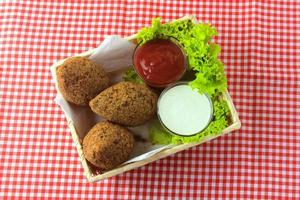 gebakken kibbeh met tomatensaus in een mand, over rustieke houten tafel foto