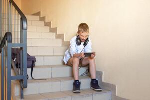 een emotioneel jongen in een overhemd is zittend Aan de trap , op zoek Bij de telefoon, geschreeuw foto