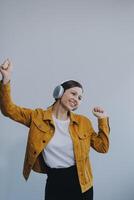 de mooi emotioneel Europese bruin haar vrouw met gezond schoon huid, charmant glimlach, gekleed in gewoontjes licht kleren, luistert en geniet muziek- Aan hoofdtelefoons met tablet Aan een wit achtergrond. foto