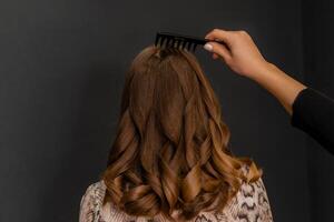 een vrouw met lang bruin haar- is krijgen haar haar- geborsteld door een ander persoon. de borstel is zwart en de vrouw haar- is krullend. foto