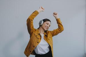 de mooi emotioneel Europese bruin haar vrouw met gezond schoon huid, charmant glimlach, gekleed in gewoontjes licht kleren, luistert en geniet muziek- Aan hoofdtelefoons met tablet Aan een wit achtergrond. foto