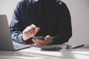 kant visie schot van een man's handen gebruik makend van slim telefoon in interieur, achterzijde visie van bedrijf Mens handen bezig gebruik makend van cel telefoon Bij kantoor bureau, jong mannetje leerling typen Aan telefoon zittend Bij houten tafel, gloed foto