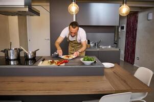 portret van een Mens in chef-kok schort, staand Bij keuken eiland en gebruik makend van keuken handdoek, afvegen weg sporen van tomaat saus Aan een bord van vers bereid spaghetti. mensen. culinair. Italiaans keuken foto