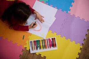 weinig meisje glimlachen tekening afbeelding, aan het liegen Aan haar buik Aan een veelkleurig puzzel tapijt. mensen. onderwijs. terug naar school- concept foto
