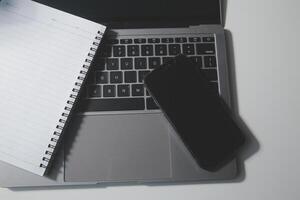 top visie van computer bureau met toetsenbord, smartphone, schrijfbehoeften en koffie beker, knipsel pad foto