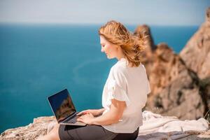 freelance vrouw werken Aan een laptop door de zee, typen weg Aan de toetsenbord terwijl genieten van de mooi visie, markeren de idee van afgelegen werk. foto