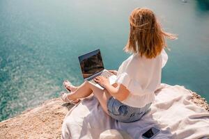freelance vrouw werken Aan een laptop door de zee, typen weg Aan de toetsenbord terwijl genieten van de mooi visie, markeren de idee van afgelegen werk. foto