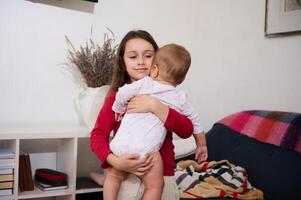 Kaukasisch mooi lief weinig kind meisje glimlacht Holding haar baby broer, nemen zorg van hem. de concept van familie relaties en zorg. Internationale kinderen dag. broer en zus samen foto